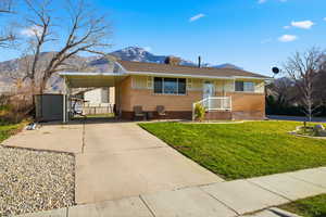 View of front of property featuring driveway, a front lawn, an attached carport, a storage shed, and brick siding