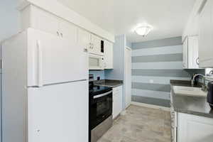 Kitchen featuring dark countertops, white appliances, white cabinets, a textured ceiling, and stone finish flooring