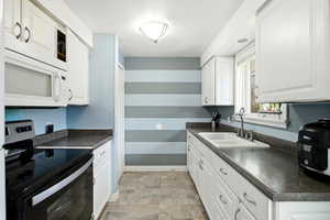 Kitchen with stainless steel electric range, dark countertops, white microwave, white cabinets, and a textured ceiling