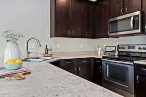 Kitchen with appliances with stainless steel finishes, dark brown cabinetry, and light stone countertops