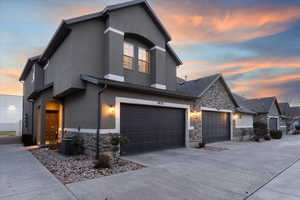 View of front of property featuring stone siding, concrete driveway, stucco siding, and an attached garage