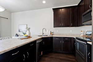 Kitchen with stainless steel appliances, dark wood finished floors, light stone counters, recessed lighting, and dark brown cabinets