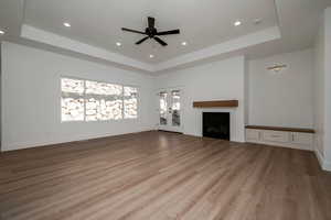Unfurnished living room featuring a raised ceiling, french doors, a fireplace, light wood-type flooring, and recessed lighting
