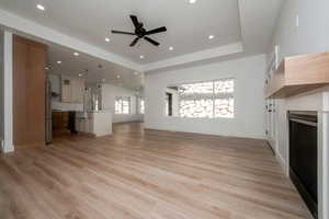 Unfurnished living room with a tray ceiling, light wood-style flooring, a fireplace, ceiling fan, and recessed lighting
