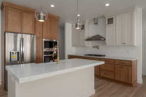 Kitchen featuring brown cabinets, glass insert cabinets, decorative light fixtures, light wood-style floors, and appliances with stainless steel finishes