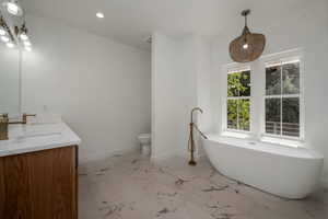 Full bathroom featuring a freestanding bath, double vanity, light marble finish floors, and recessed lighting