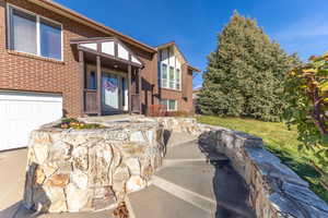 Doorway to property featuring brick siding, a lawn, and a garage