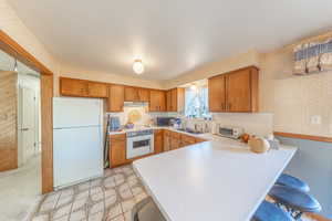 Kitchen featuring wallpapered walls, light countertops, white appliances, brown cabinets, and a breakfast bar area