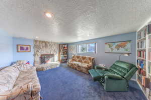 Carpeted living room with a textured ceiling, recessed lighting, and a stone fireplace