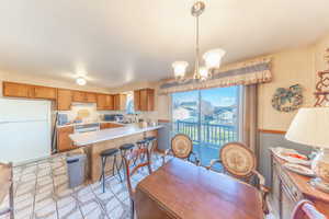 Kitchen featuring wallpapered walls, light countertops, white appliances, brown cabinetry, and a breakfast bar area