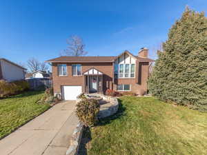 View of front of home featuring brick siding, a chimney, driveway, and an attached garage