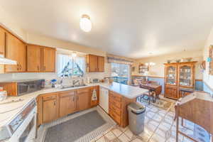 Kitchen featuring wallpapered walls, a peninsula, a wainscoted wall, light countertops, and brown cabinetry