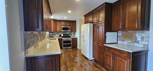 Kitchen featuring appliances with stainless steel finishes, backsplash, light stone countertops, dark wood-style floors, and recessed lighting