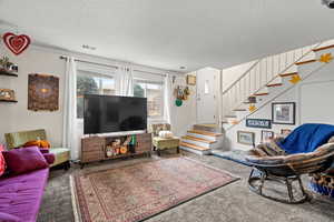 Carpeted living room with a textured ceiling and stairway