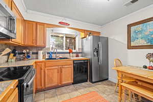 Kitchen featuring crown molding, appliances with stainless steel finishes, a textured ceiling, decorative backsplash, and brown cabinets