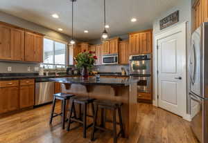 Kitchen with a breakfast bar, appliances with stainless steel finishes, pendant lighting, a center island, and brown cabinets
