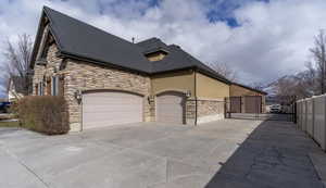 View of home's exterior with stone siding, driveway, a gate, an attached garage, and stucco siding