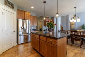 Kitchen featuring stainless steel fridge with ice dispenser, brown cabinets, light wood-style flooring, hanging light fixtures, and a textured ceiling