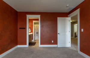Unfurnished bedroom featuring light colored carpet, ensuite bathroom, and a textured ceiling