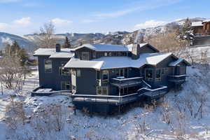 Snow covered house with a chimney and a deck with mountain view