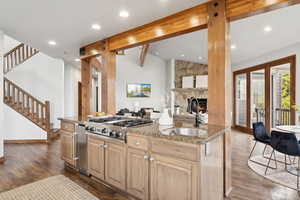 Kitchen featuring light stone countertops, an island with sink, dark wood-style flooring, a stone fireplace, and recessed lighting