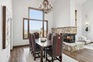 Dining space featuring a stone fireplace, high vaulted ceiling, wood finished floors, and a chandelier