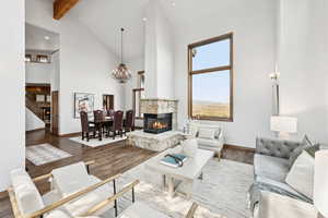 Living room featuring a stone fireplace, a chandelier, beamed ceiling, high vaulted ceiling, and recessed lighting