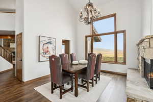 Dining area with a fireplace, high vaulted ceiling, wood-type flooring, a chandelier, and stairway