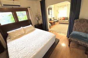 Bedroom with light wood-style flooring, arched walkways, and a wall mounted AC
