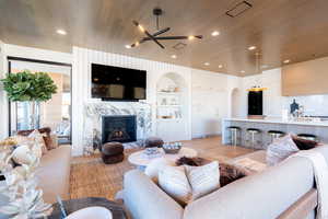 Living room featuring a premium fireplace, built in features, light wood finished floors, arched walkways, and wood ceiling