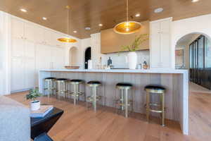 Kitchen with arched walkways, white cabinets, a kitchen bar, recessed lighting, and light wood finished floors