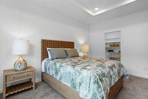 Carpeted bedroom featuring baseboards and a tray ceiling