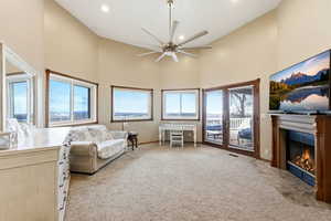 Living area with a towering ceiling, a fireplace with flush hearth, light carpet, ceiling fan, and recessed lighting