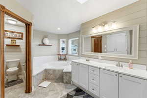 Full bathroom with double vanity, a bath, wooden walls, and recessed lighting