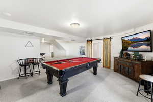 Rec room with a barn door, billiards table, light carpet, and a textured ceiling