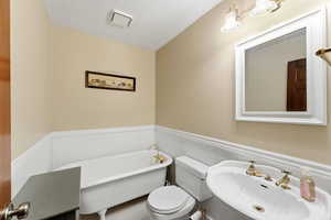 Full bath featuring a wainscoted wall, a soaking tub, a textured ceiling, and a decorative wall