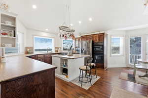 Kitchen featuring open shelves, a kitchen island, dark wood-style floors, light countertops, and healthy amount of natural light