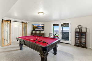 Playroom featuring a barn door, a textured ceiling, pool table, and light colored carpet
