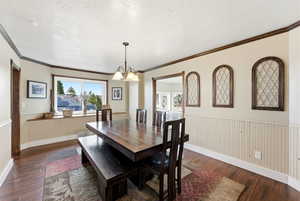 Dining space with wainscoting, dark wood-type flooring, a textured ceiling, a chandelier, and ornamental molding