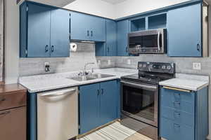 Kitchen featuring blue cabinets, stainless steel appliances, open shelves, and light countertops