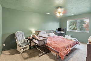 Bedroom with a textured ceiling, carpet floors, and ceiling fan