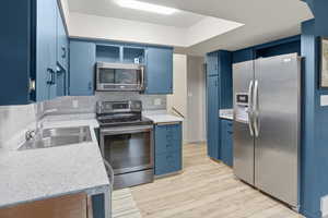 Kitchen with blue cabinets, open shelves, appliances with stainless steel finishes, backsplash, and light wood-style floors