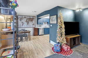 Kitchen with decorative backsplash, light countertops, blue cabinetry, dishwasher, and light wood-style flooring