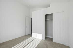 Unfurnished bedroom with light carpet, a closet, and high vaulted ceiling