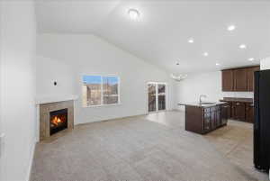 Kitchen with dark brown cabinets, a center island with sink, freestanding refrigerator, a tiled fireplace, and open floor plan