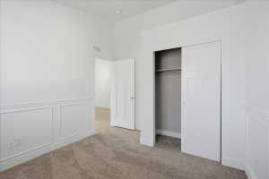 Unfurnished bedroom with a decorative wall, wainscoting, a closet, and light colored carpet