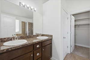 Full bath featuring a stall shower, double vanity, a walk in closet, light colored carpet, and light tile patterned floors