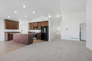 Kitchen with black appliances, light colored carpet, a kitchen island with sink, open floor plan, and dark stone countertops