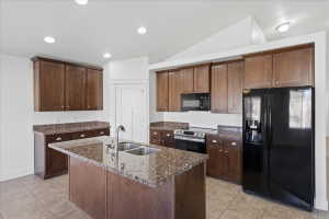 Kitchen featuring black appliances, dark stone counters, recessed lighting, an island with sink, and light tile patterned flooring