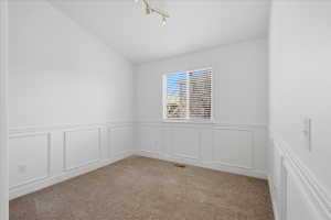 Carpeted spare room featuring vaulted ceiling, a decorative wall, and a wainscoted wall